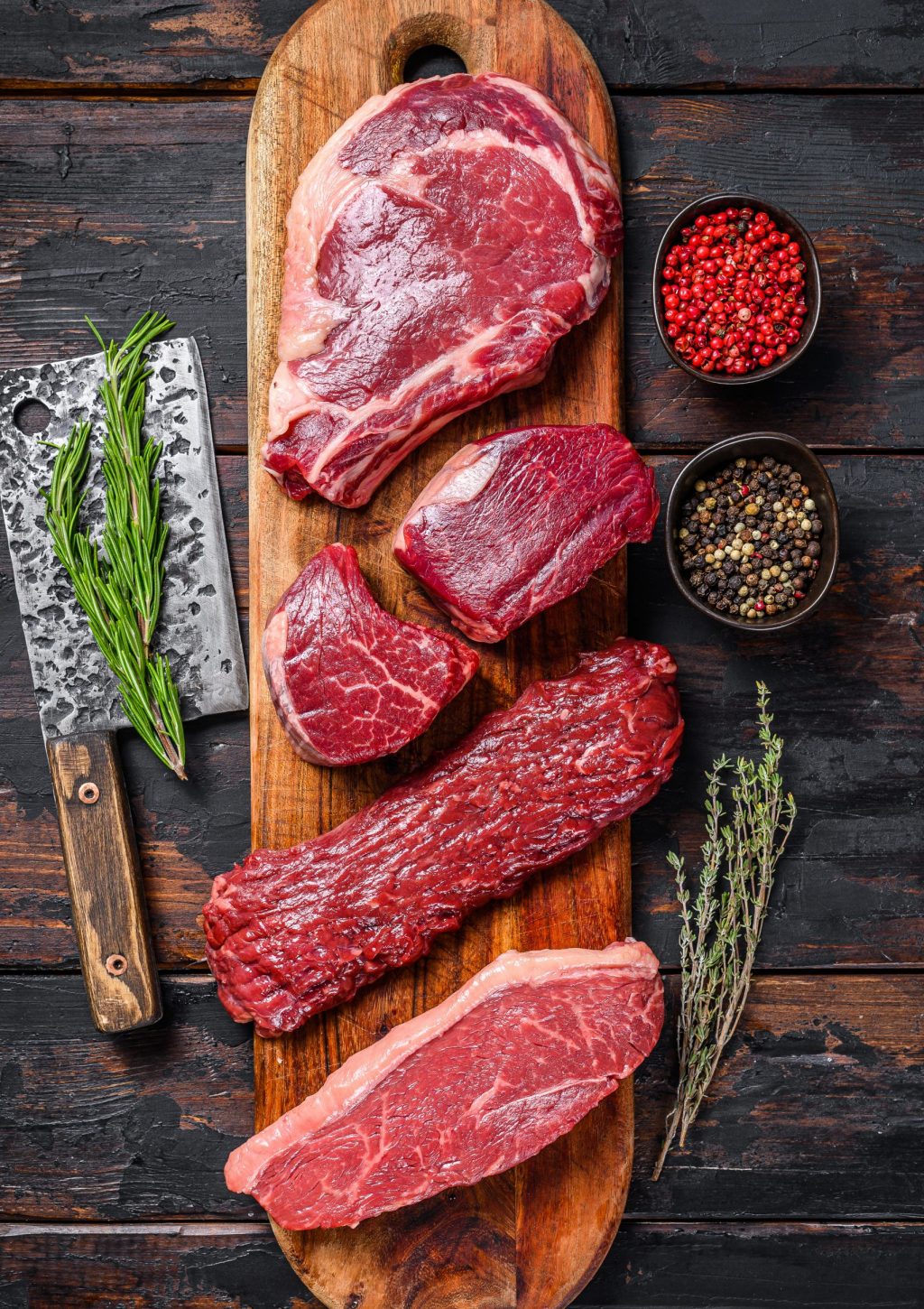 Raw prime black angus beef steaks fillet Mignon, rib eye or cowboy, Striploin or new york, skirt or machete. Wooden dark background. Top view.