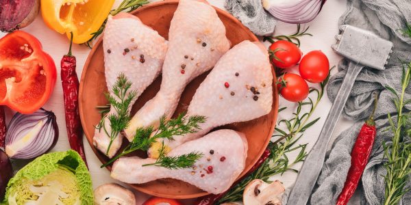 Raw chicken legs with fresh vegetables and rosemary and spices on a white wooden background. Top view. Free space for text.